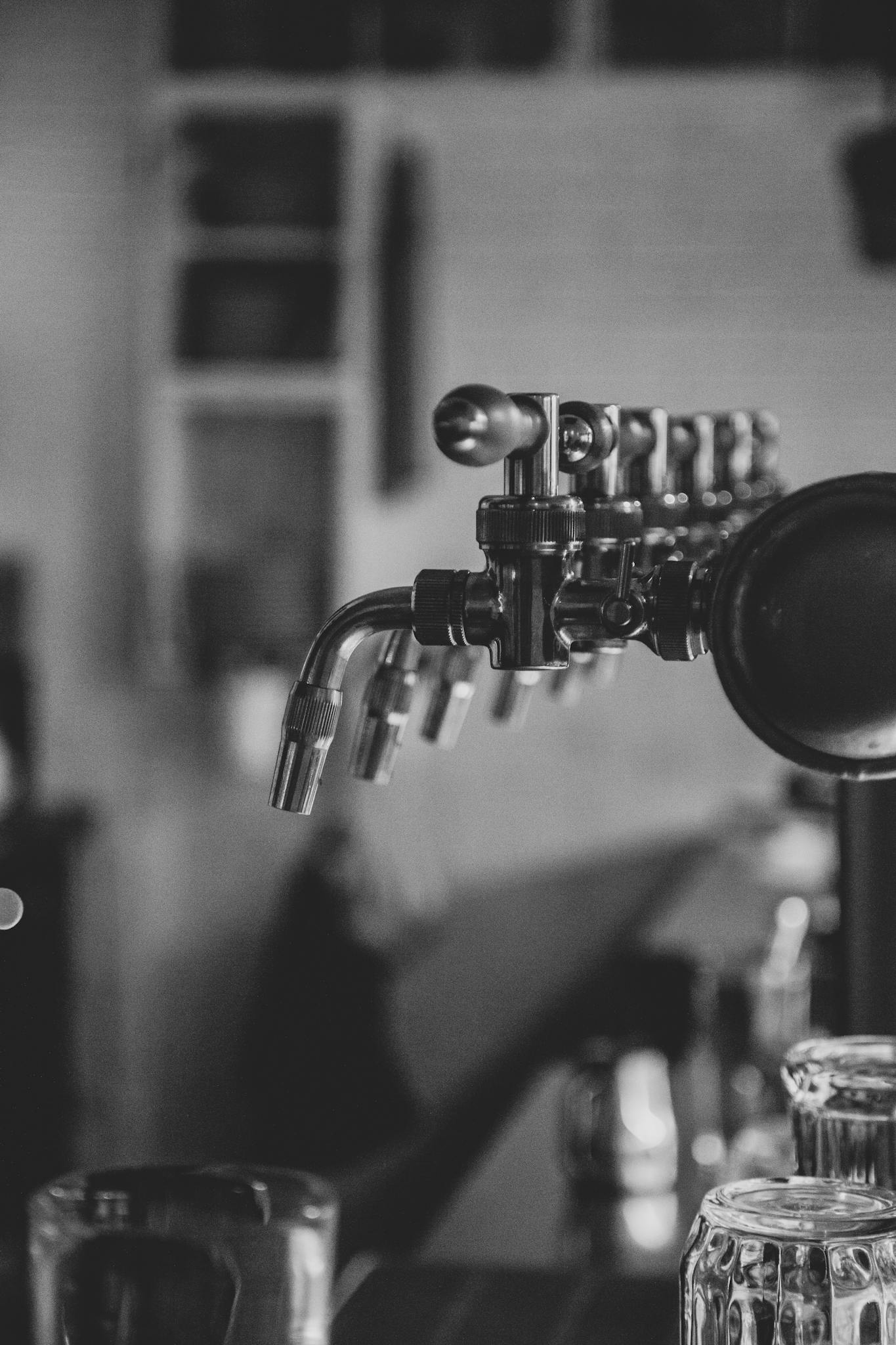 Black-and-white photo of industrial beer taps inside a cozy pub.